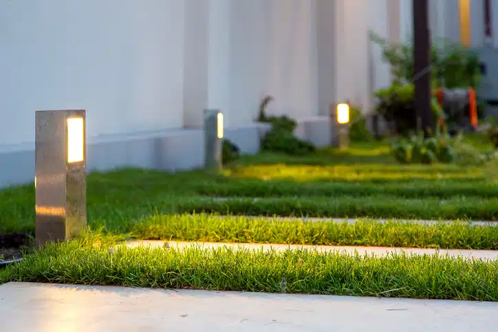 ground lantern lighting marble walkway in the evening park with a green lawn, closeup lantern illumination warm light marble pavement.
